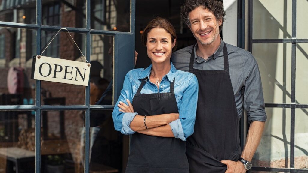 A woman and a man stand in front of a shop next to an 'open' sign